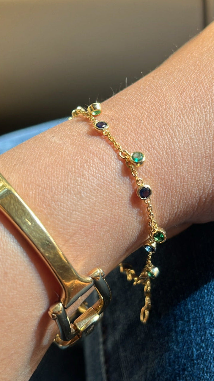 Gold bracelet with green gemstones on a wrist against a blurred background