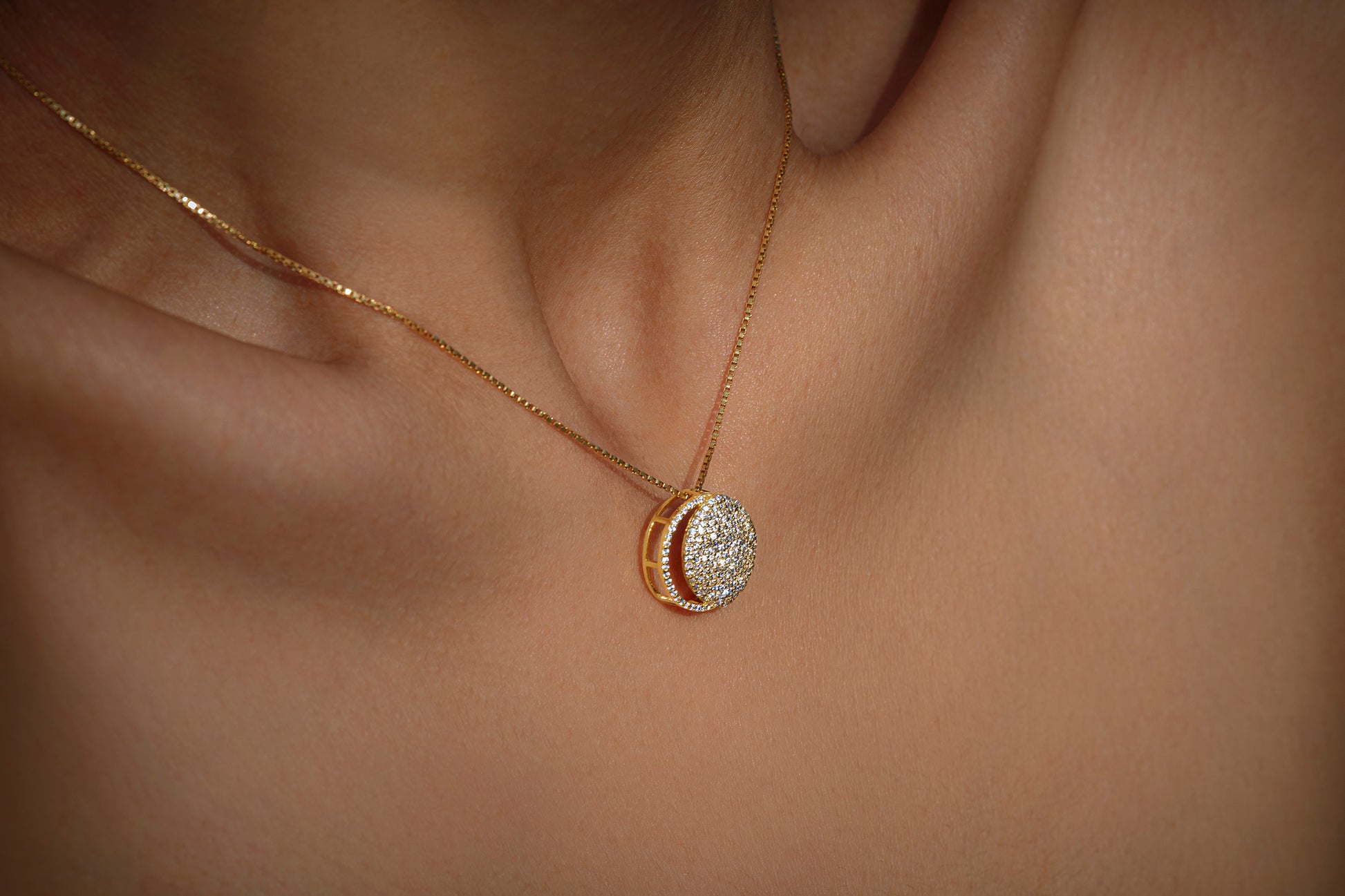 Gold necklace with diamonds in a circular pendant representing the waning crescent moon on a light gray background