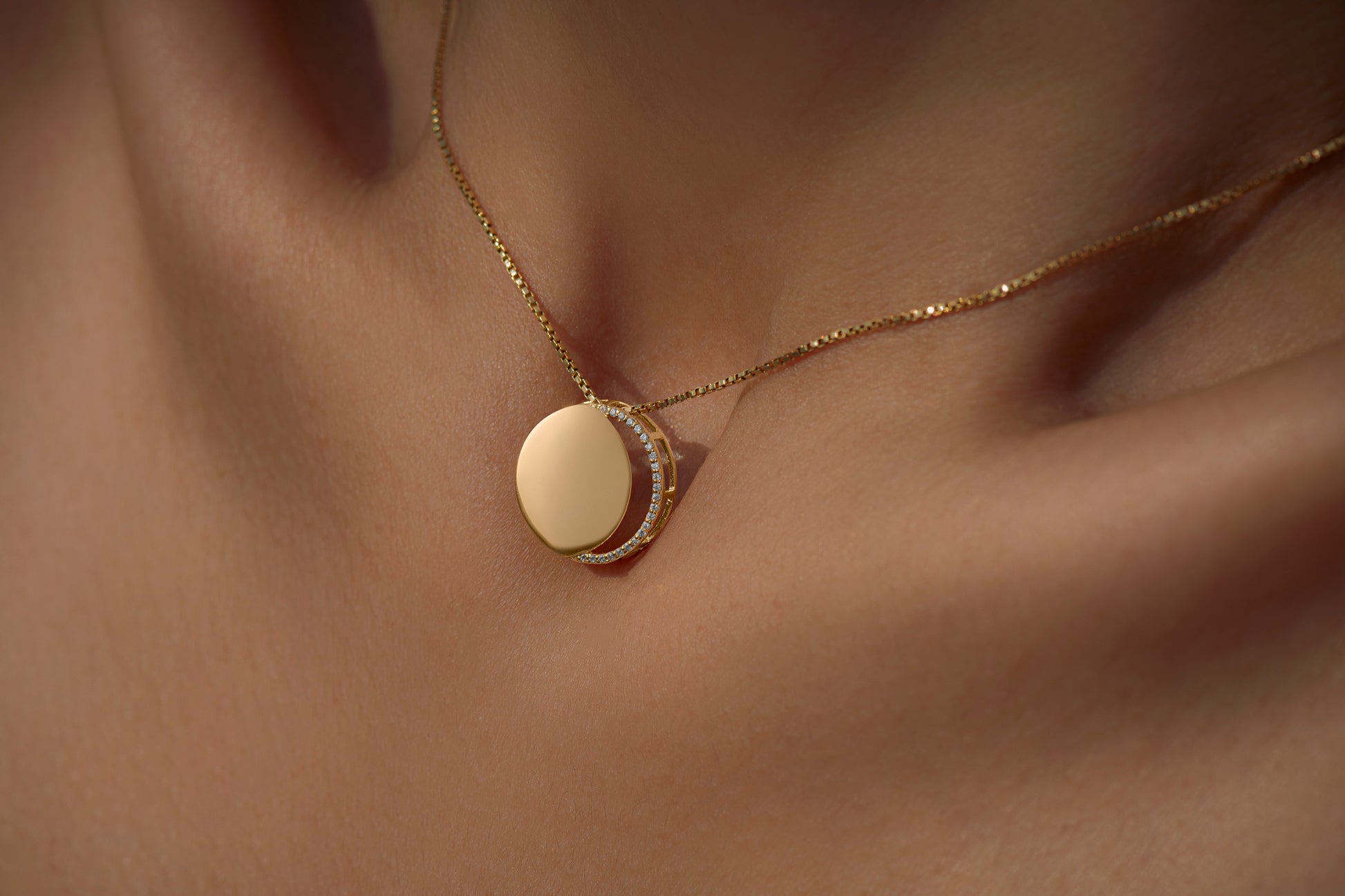 Gold necklace with diamonds in a circular pendant representing the waxing crescent moon on a light gray background