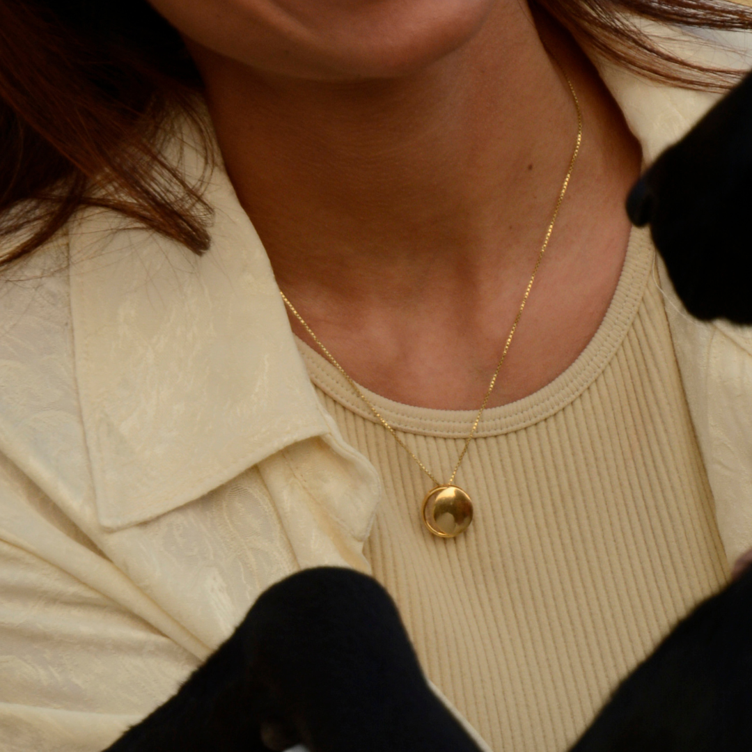 A person wearing a sterling silver pendant with a crescent shape and a high polish finish, accompanied by a chain. 